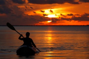 woman on kayak rowing at sunset in the ocean